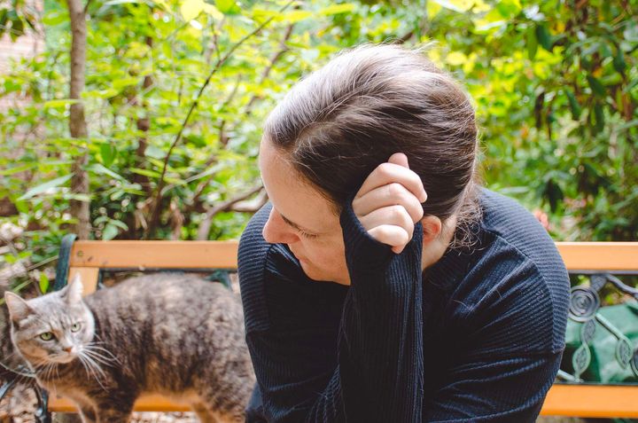 A portrait of Penny Johnson. She sits on a bench, arm holding her head up, as she looks backward toward a grey cat.