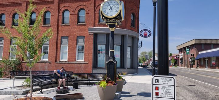 An ornate clock at the center of the photo, with a woman sitting on a metal bench playing guitar.