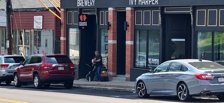 A street musician in front of a storefront, flanked by two parked vehicles.