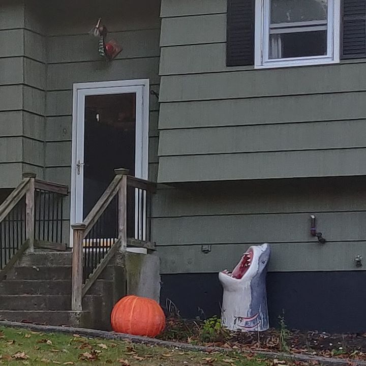 A decorative shark next to a decorative pumpkin in front of a house.