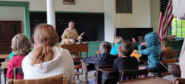 A woman dressed as an 1860s teacher instructs some children in desks. Photo courtesy Jeff Raymond.